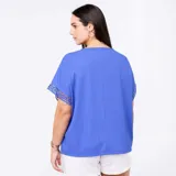 Camiseta azul con cuello redondo, mangas cortas holgadas y detalles de encaje y macramé en las costuras de las mangas.