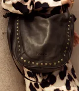 Cartera de cuero roja con tachas plateadas en el borde inferior, doble asa de cuero y cierre superior.