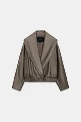 Cazadora Zara Woman Collection de efecto piel con cuello solapa ancho, manga larga, bolsillos delanteros y bajo elástico. Presenta un cierre frontal cruzado con botón a presión.