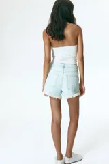 Short denim de cinco bolsillos confeccionado en algodón rígido, con diseño de tiro súper alto, detalles de roturas y desgastes, cierre frontal con botón y terminaciones deshilachadas.