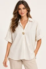 Camisa de algodón color marfil, de corte holgado, con mangas cortas con vuelta y un elegante botón decorativo dorado en el frente que cierra el escote en V.