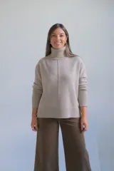 Polerón de cuello alto en color beige, con costura central vertical y puños acanalados.