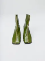 Botas de caña media color verde oliva, con punta cuadrada y taco de madera. Presentan un detalle de costura decorativa en color contrastante a lo largo del empeine y cierre posterior.