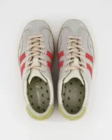 Championes de estilo retro con capellada de gamuza en tono gris claro, detalles laterales en rojo y refuerzo en el talón color verde lima. Presenta suela de goma color caramelo y cierre mediante cordones.