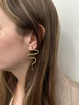 Set de accesorios compuesto por un collar, un brazalete y dos pares de aros, todos elaborados en bronce, presentados en un sobre de cuero marrón tipo gamuza.