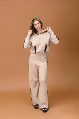 Conjunto de dos piezas en color beige con detalles en negro, compuesto por un buzo con capucha y cierre frontal, y un pantalón de corte recto y holgado. Ambas prendas presentan franjas laterales en contraste.