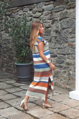 Vestido largo de tejido de punto, con rayas horizontales en tonos tierra, azul y blanco. Presenta cuello redondo, mangas cortas caídas y aberturas laterales en el ruedo.