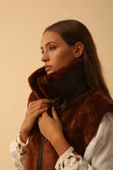 Chaleco de piel sintética en color chocolate, con cierre frontal y detalles de cuero en los bordes. Presenta un diseño de cuello solapa y ajuste lateral con hebillas.