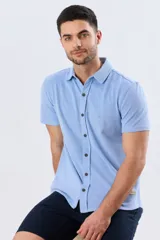 Camisa de piqué lisa color celeste, de manga corta, con cuello camisero y cierre frontal de botones oscuros.