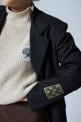 Sweater de punto grueso color crema, con cuello alto y parche circular con bordado en el pecho.