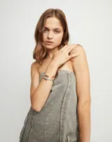 Pulsera rígida de aleación de metales bañada en plata de ley, con diseño abierto y logo de la marca grabado en uno de los extremos.