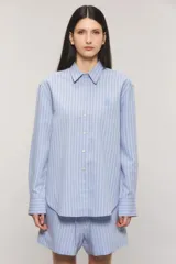 Camisa Sailor Line de calce holgado y diseño a rayas. Presenta cuello camisero, mangas largas y puños abotonados. Cuenta con acceso frontal mediante botones a tono y detalle bordado en el pecho.