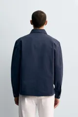 Sobrecamisa de corte regular confeccionada en tejido de algodón con estructura canvas, color negro. Presenta cuello solapa, manga larga con puño abotonado, un bolsillo frontal de plastrón y cierre frontal con botonadura oculta.