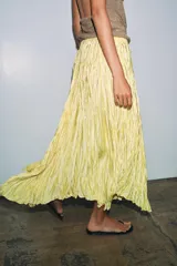 Falda larga de tiro medio color amarillo, con cintura elástica, diseño plisado y bajo asimétrico.