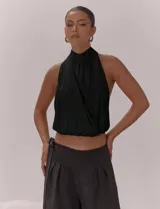 Top negro con escote halter y cuello alto. Presenta un diseño cruzado en el frente con pliegues, espalda descubierta con lazo regulable y bajo con terminación elástica.
