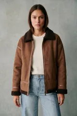 Campera tipo gamulán de corte oversize, color marrón con interior y cuello de corderito sintético oscuro. Presenta cierre frontal, detalles de costuras reforzadas y terminaciones en puños y ruedo con corderito a la vista.