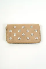 Billetera rectangular color camel con cierre perimetral y tachas metálicas plateadas dispuestas en toda la superficie frontal.