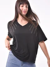 Remera blanca de manga corta con cuello en V y apliques de tachas metálicas doradas dispuestas en forma de V invertida en la zona de los hombros.