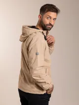 Campera de nylon con capucha, cierre frontal y forro de red. Presenta un diseño minimalista en color beige con detalles en negro.