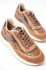 Championes deportivos en tonos marrón y caramelo con estampado de serpiente y detalles en charol. Cuenta con cordones marrones y suela de goma blanca con base dentada.