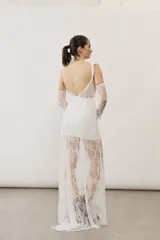 Vestido largo blanco de encaje con diseño asimétrico, tirante fino en un hombro y falda transparente.