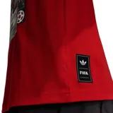Remera de algodón color rojo con corte holgado, cuello redondo y mangas cortas. Presenta el logo de Adidas Originals bordado en el pecho y una etiqueta decorativa en el ruedo inferior.
