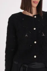 Saco de punto negro con diseño bordado floral en relieve, cuello redondo, cierre frontal con botones metálicos y bolsillos frontales decorativos.