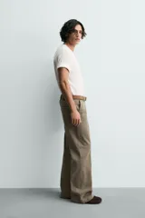 Pantalón de denim color verde oliva, estilo chino con corte ancho y bota acampanada (flare) desde la rodilla. Tiro medio, confeccionado en tejido rígido. Presenta bolsillos frontales y bolsillos traseros de plastrón.