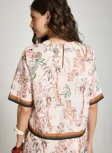 Blusa estampada Le Lis Blanc con diseño de paisaje tropical y arquitectónico, cuello redondo y mangas cortas con ribetes en tonos marrón y negro.