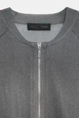 Chaqueta estilo bomber de punto color beige con acabado brillante, cuello redondo, manga larga con puños elásticos y cierre frontal con cremallera.