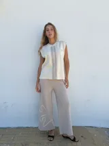 Pantalón de punto color beige, de corte ancho y largo hasta el tobillo, con diseño abstracto bordado en blanco en la parte inferior de la pierna izquierda.