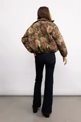 Campera tipo bomber con diseño de estampado floral estilo tapicería sobre fondo negro. Presenta cuello clásico, cierre frontal con botones metálicos, bolsillos laterales y puños elásticos.