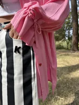 Camisa oversize de fibrana color rosa con botones rojos en forma de corazón y mangas largas con ajuste en los puños.