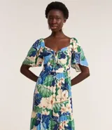 Vestido largo de viscosa con estampado tropical de flores blancas y hojas verdes y azules. Presenta escote cuadrado con lazo ajustable en el centro del busto y mangas cortas abullonadas. La falda es escalonada con volados.