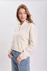 Campera de polar en color crudo, con cuello alto, cierre frontal completo y bolsillos laterales.