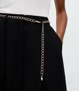 Pantalón de sastrería modelo aladim, color negro, confeccionado en crepé. Presenta pliegues en la cintura, corte holgado con piernas anchas que se estrechan en los tobillos y detalle de cinturón de cadena metálica.