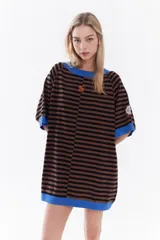 Vestido corto holgado de punto a rayas horizontales marrones y negras, con cuello, dobladillo de mangas y ruedo en color azul. Presenta un pequeño bordado en naranja en el pecho y un parche en la manga.