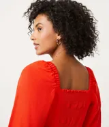 Blusa cropped roja de lino y viscosa, con escote cuadrado, mangas largas abullonadas y lazo frontal.