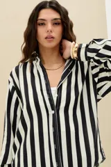 Camisa oversize de manga larga a rayas verticales en color negro y blanco, con cuello camisero y cierre frontal con botones.