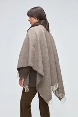 Ruana de lana sin teñir en tonos beige, con textura acanalada y terminaciones con flecos en los bordes.