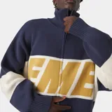 Buzo tejido de punto con cierre frontal metálico, cuello polo y diseño oversize. Presenta bloques de color en azul marino, blanco y amarillo con el logo de la marca tejido en técnica jacquard en el frente.