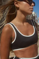 Conjunto de bikini negro con textura y vivos blancos. El corpiño es estilo top de escote redondo y breteles fijos anchos. La bombacha es de tiro alto.