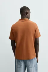 Polo de manga corta color blanco roto, con cuello solapa y cierre frontal de cremallera. Presenta un tejido de piqué estructurado y corte regular fit.