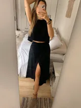 Conjunto de dos piezas compuesto por un top corto sin mangas y una pollera larga con tajo lateral. El top presenta un diseño minimalista y la pollera es ajustable en la cintura.