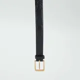 Cinturón negro con hebilla dorada y estampado de cocodrilo.