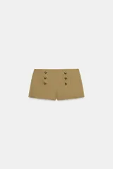 Shorts mini de tiro alto en color beige, confeccionados en mezcla de algodón, con doble hilera de botones metálicos dorados en la parte frontal y cierre lateral con cremallera oculta.