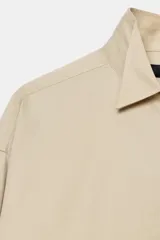 Camisa oversize color beige con mezcla de algodón, cuello smoking, manga larga con puños anchos y cierre frontal con botones ocultos por solapa.
