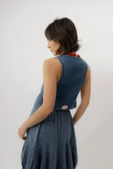 Chaleco de denim azul con cuello en V, cierre frontal con botones metálicos y pespuntes en contraste.
