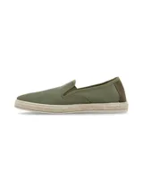 Alpargatas tipo slip-on color verde oliva, confeccionadas con materiales reciclados. Presentan un diseño con detalle bordado de espina de pescado en el lateral, refuerzo de gamuza en el talón y suela con borde de yute trenzado.