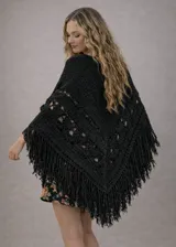 Ruana tejida en lana merino color crudo, con diseño calado, terminación en flecos y caída envolvente.